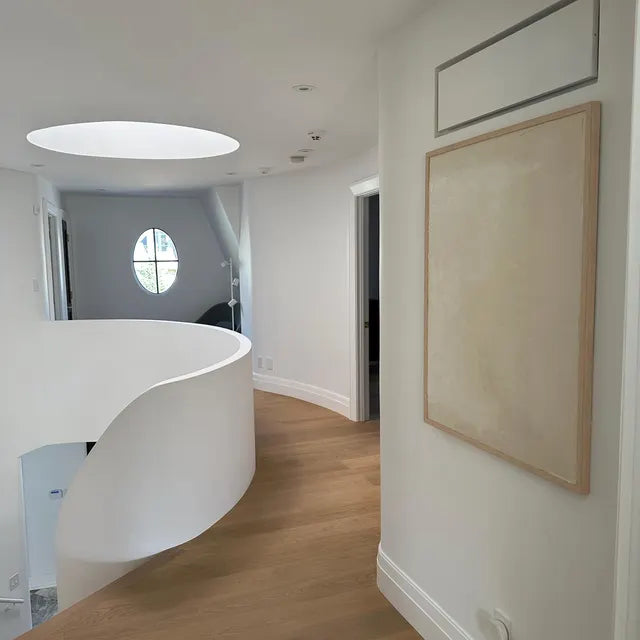 A minimalist abstract artwork displayed on a wall in a modern interior space, with a neutral beige tone and a simple, subtle design.