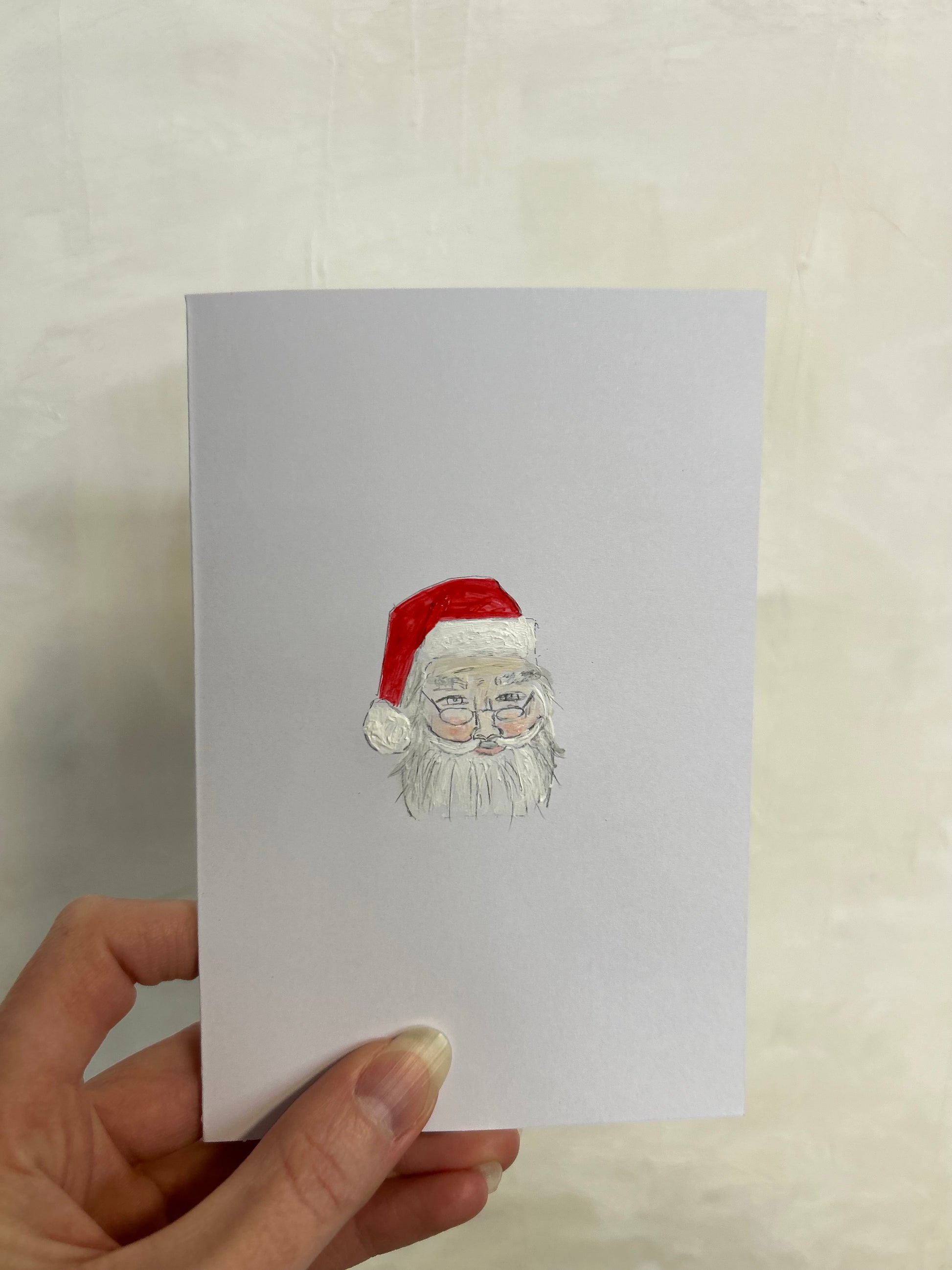 Hand holding a card with a Santa Claus illustration on a light background