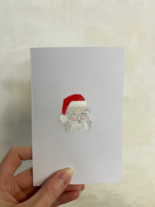 Hand holding a card with a Santa Claus illustration on a light background